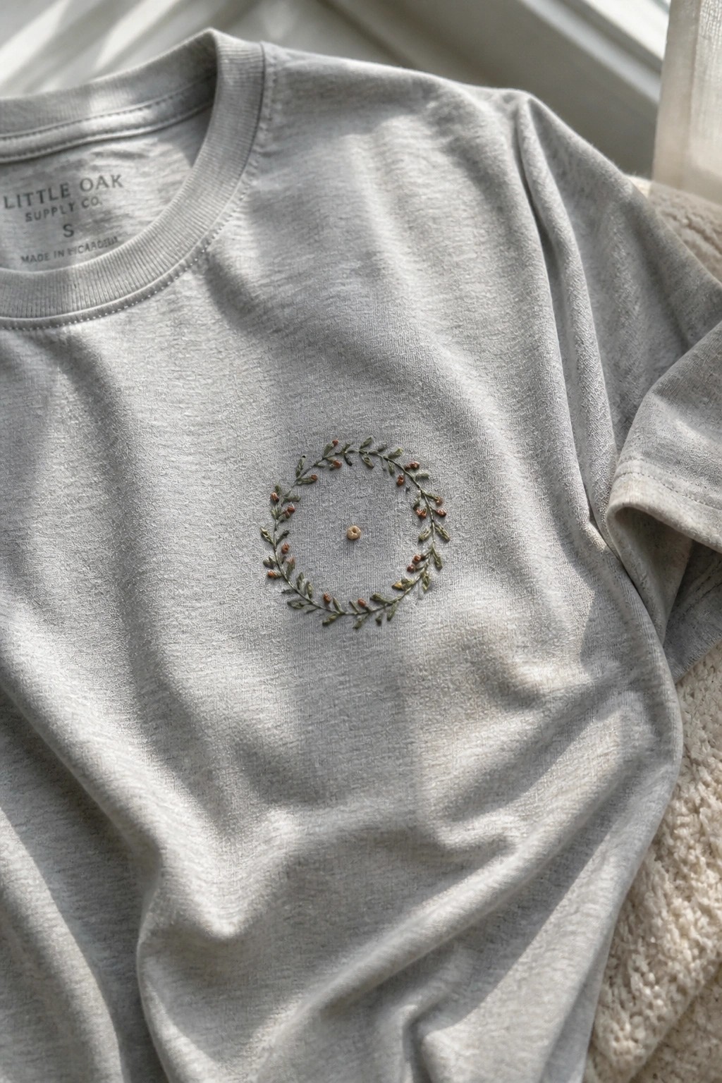 Light gray t-shirt with embroidered green wreath and rust berries on chest