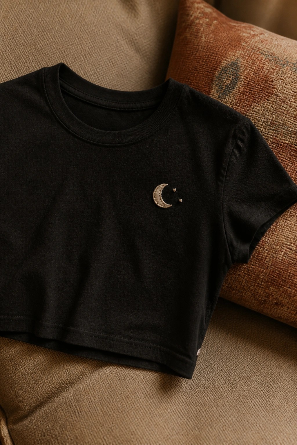 Black cropped t-shirt with embroidered crescent moon and stars on brown cushions.