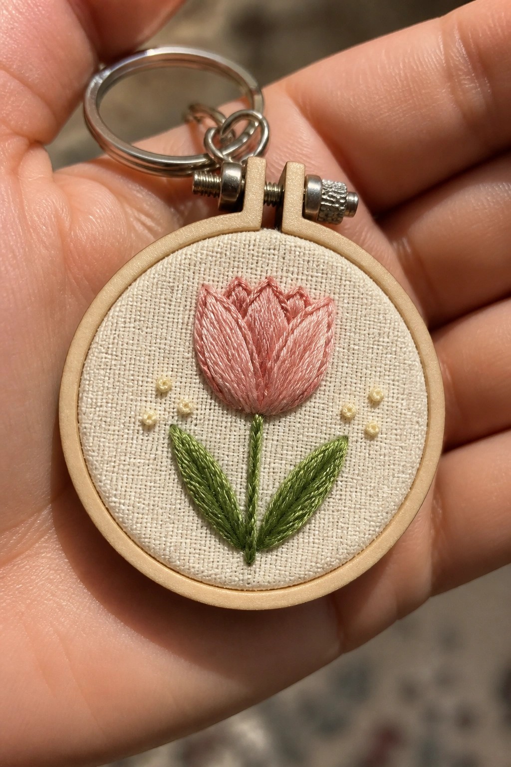 Hand holding keychain with pink tulip embroidered in tiny wooden hoop.