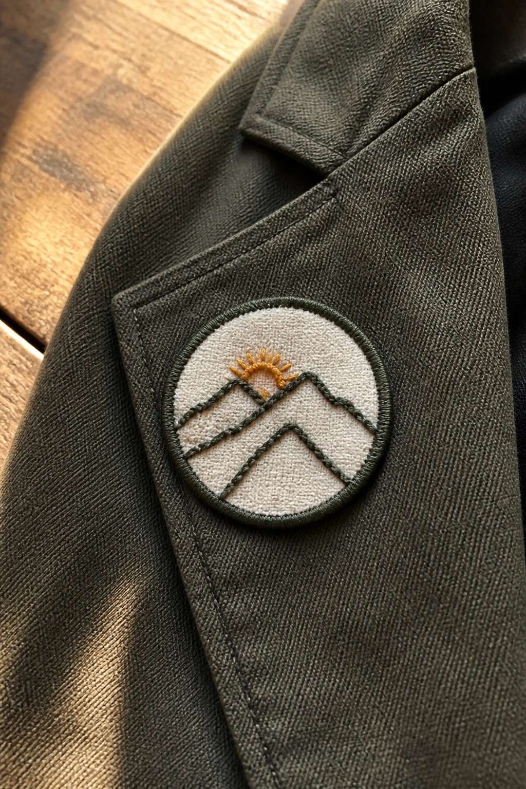 Embroidered patch with green mountains and yellow sun on dark green jacket