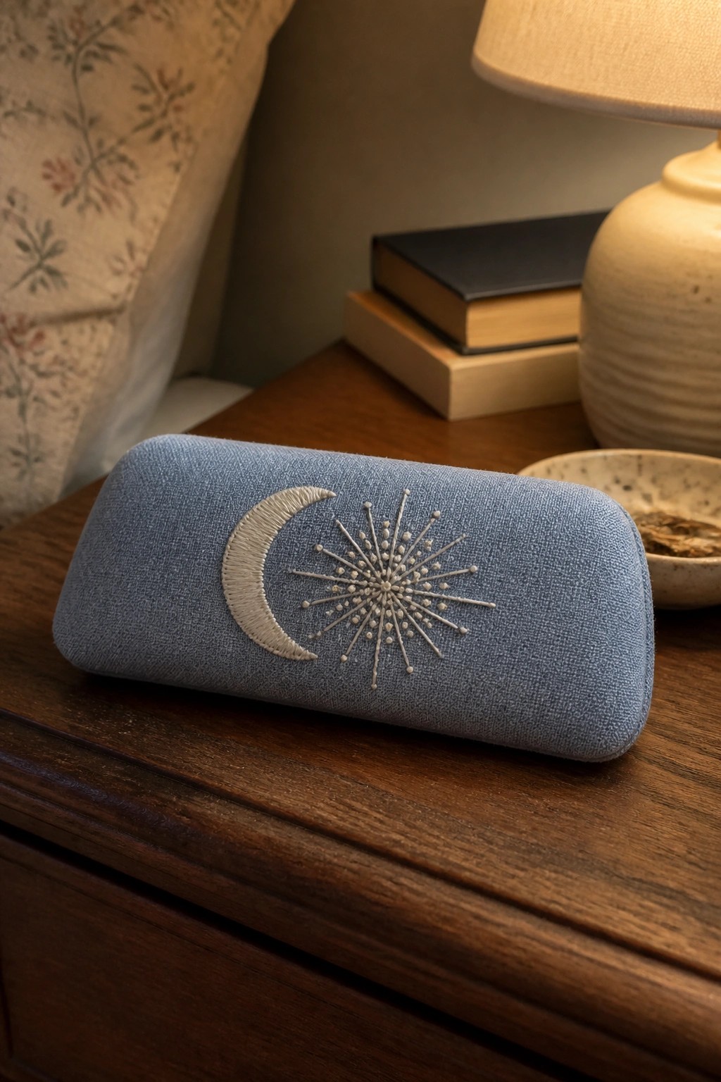 Blue fabric glasses case with embroidered crescent moon and starburst design on a wooden surface.