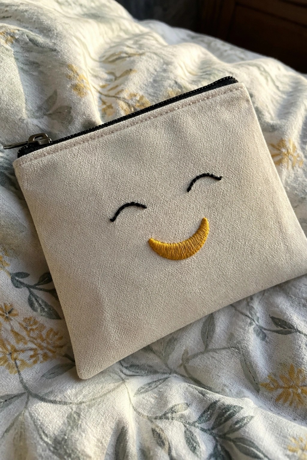 White zippered pouch with black eyes and yellow smile on floral bedding