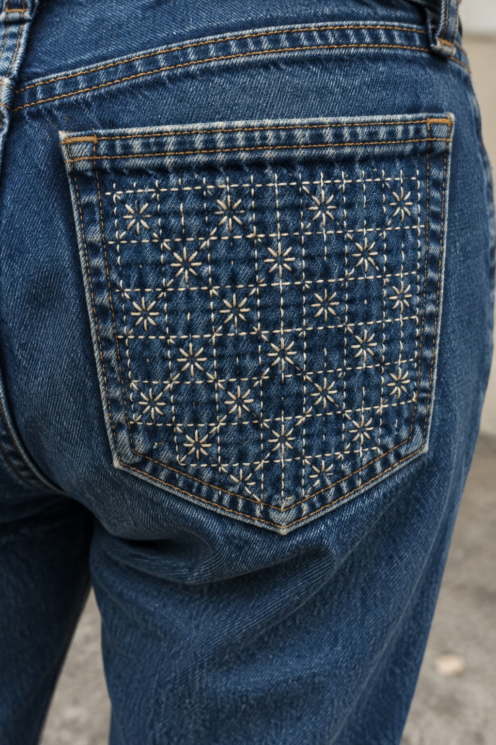 Cream geometric flower and dash embroidery covers the back pocket of blue jeans.