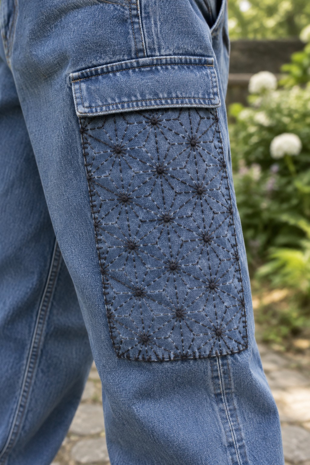 Dark geometric starburst stitching covers a long rectangular patch on the leg of blue jeans.