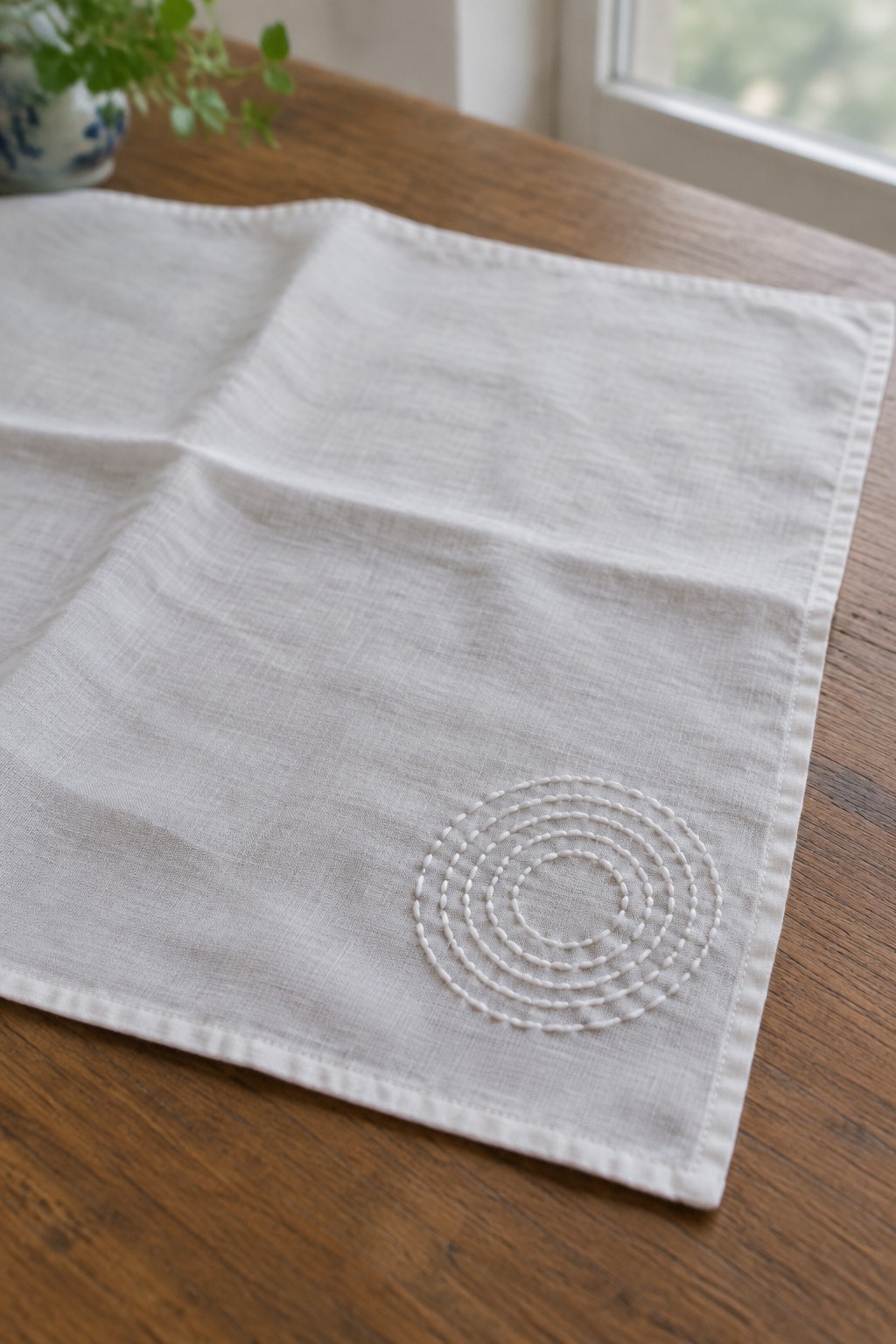 White concentric stitched circles decorate one corner of a white linen runner on a wooden table.