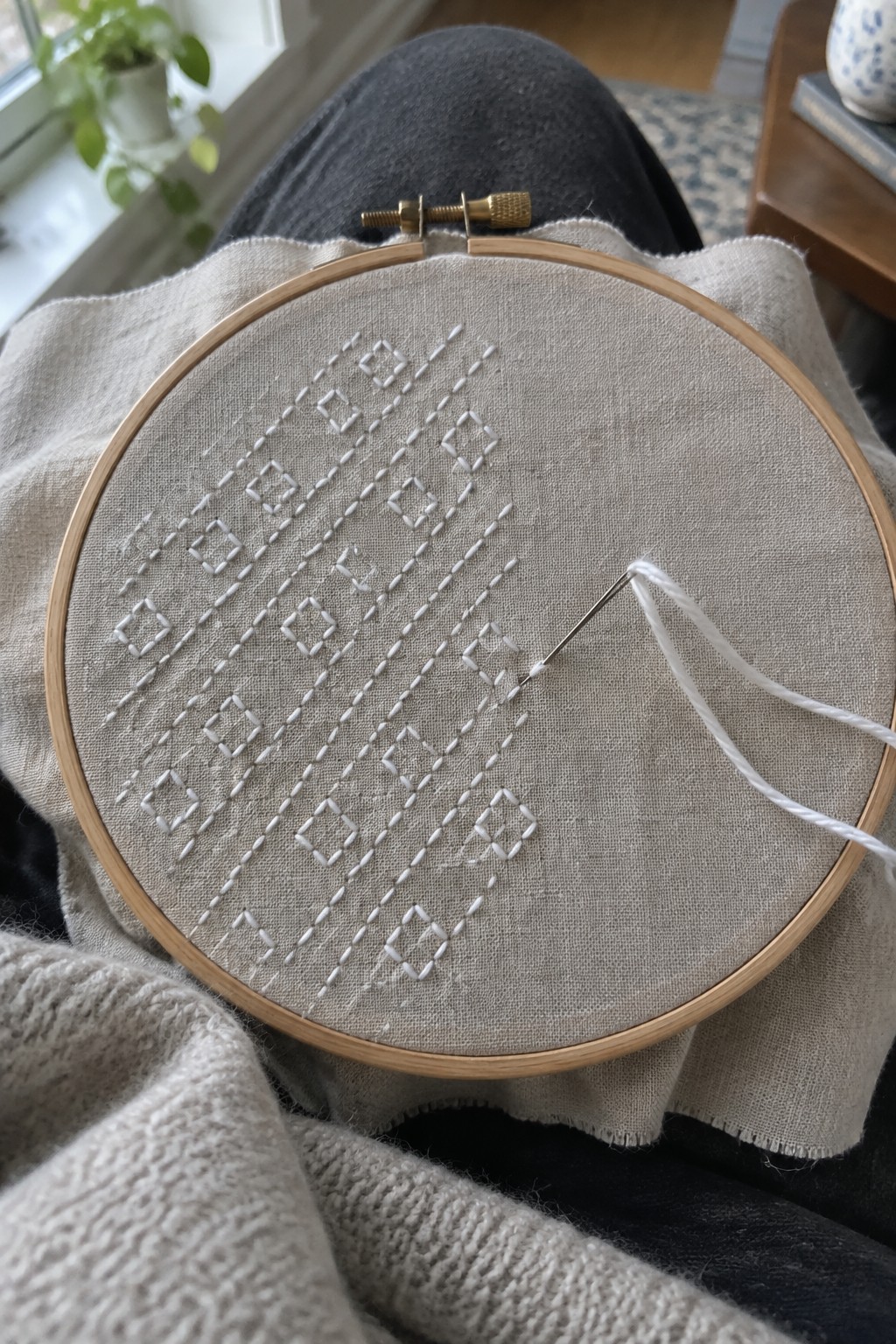 White running stitches form diagonal rows of diamond motifs and parallel lines on linen held in an embroidery hoop.