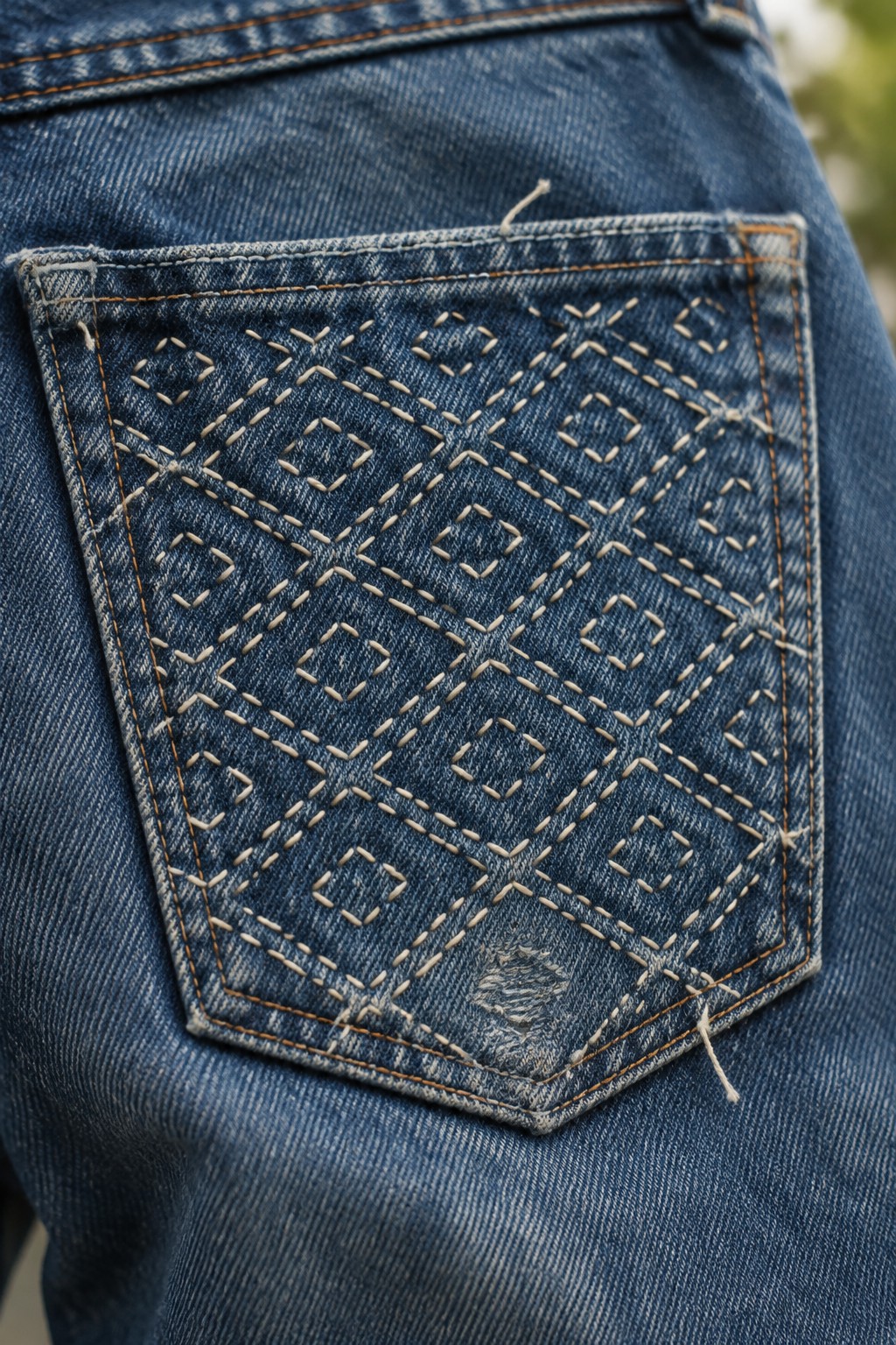 Light running stitches form layered diamond patterns across the back pocket of blue jeans.