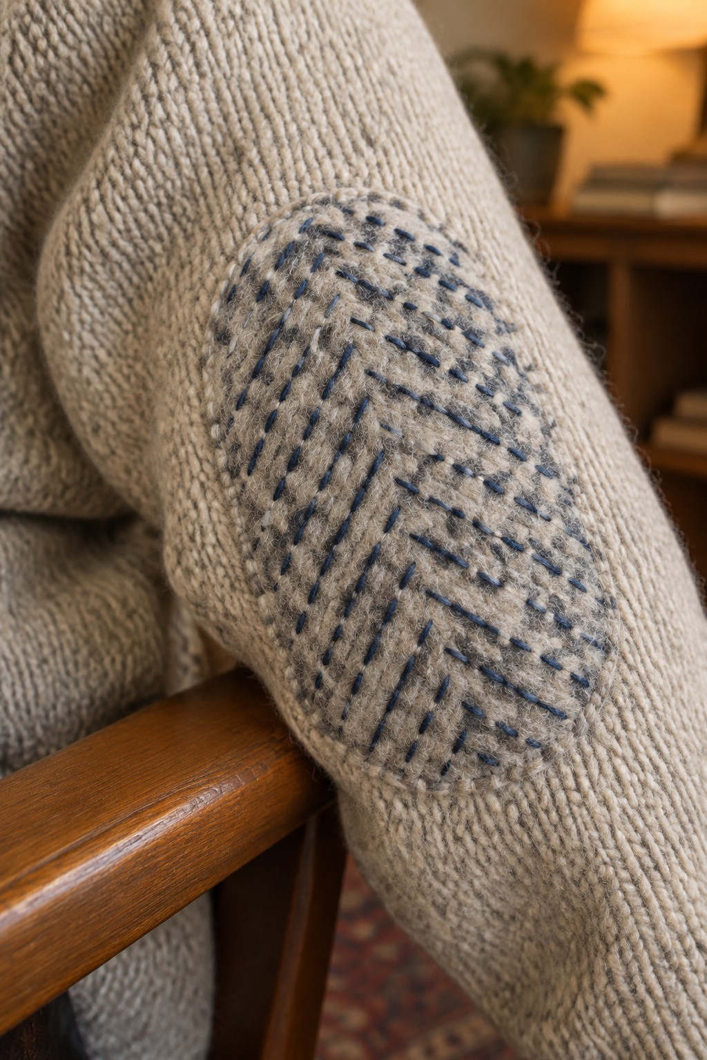 Blue running stitches form a rounded patch on the elbow of a beige knit sweater.