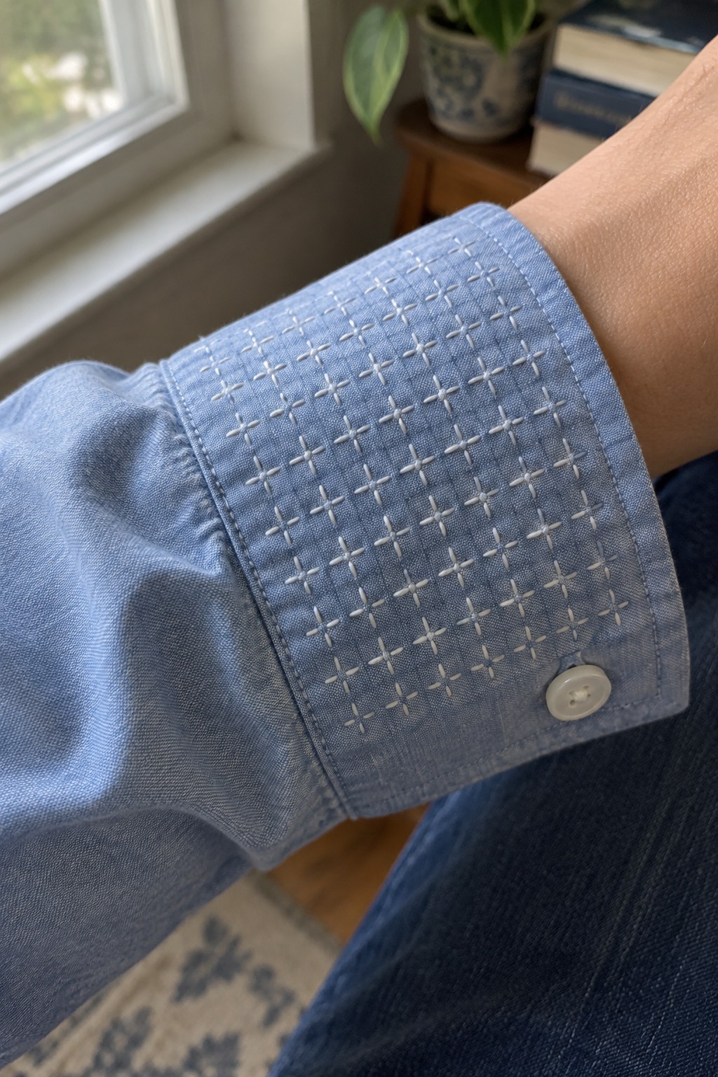 White cross-shaped embroidery covers the cuff of a blue shirt.