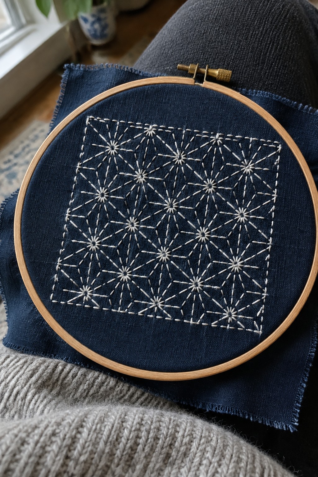 White geometric starburst stitching covers a square of dark blue fabric held in an embroidery hoop.