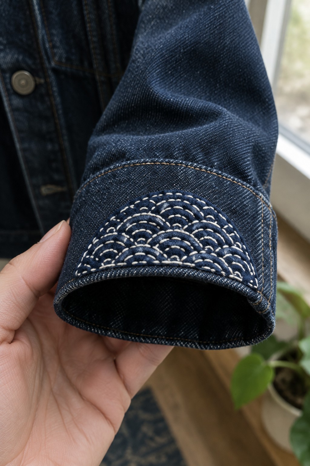 A dark denim jacket cuff with a cream arched sashiko pattern stitched across a patch.