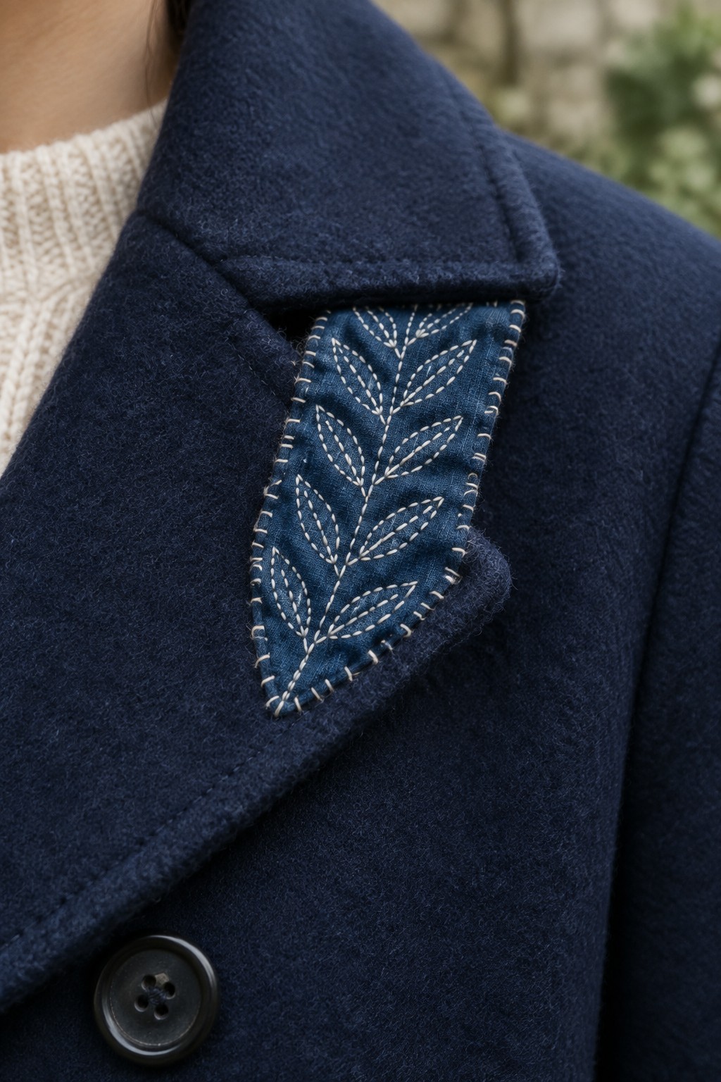 Close-up of a navy coat with a blue leaf-pattern sashiko patch tucked into its breast pocket.
