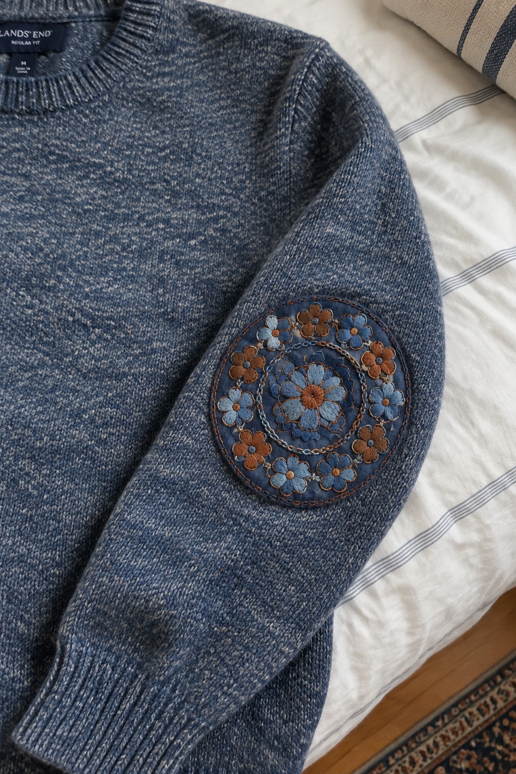 A blue sweater sleeve with a circular blue-and-rust floral embroidery patch on the elbow.