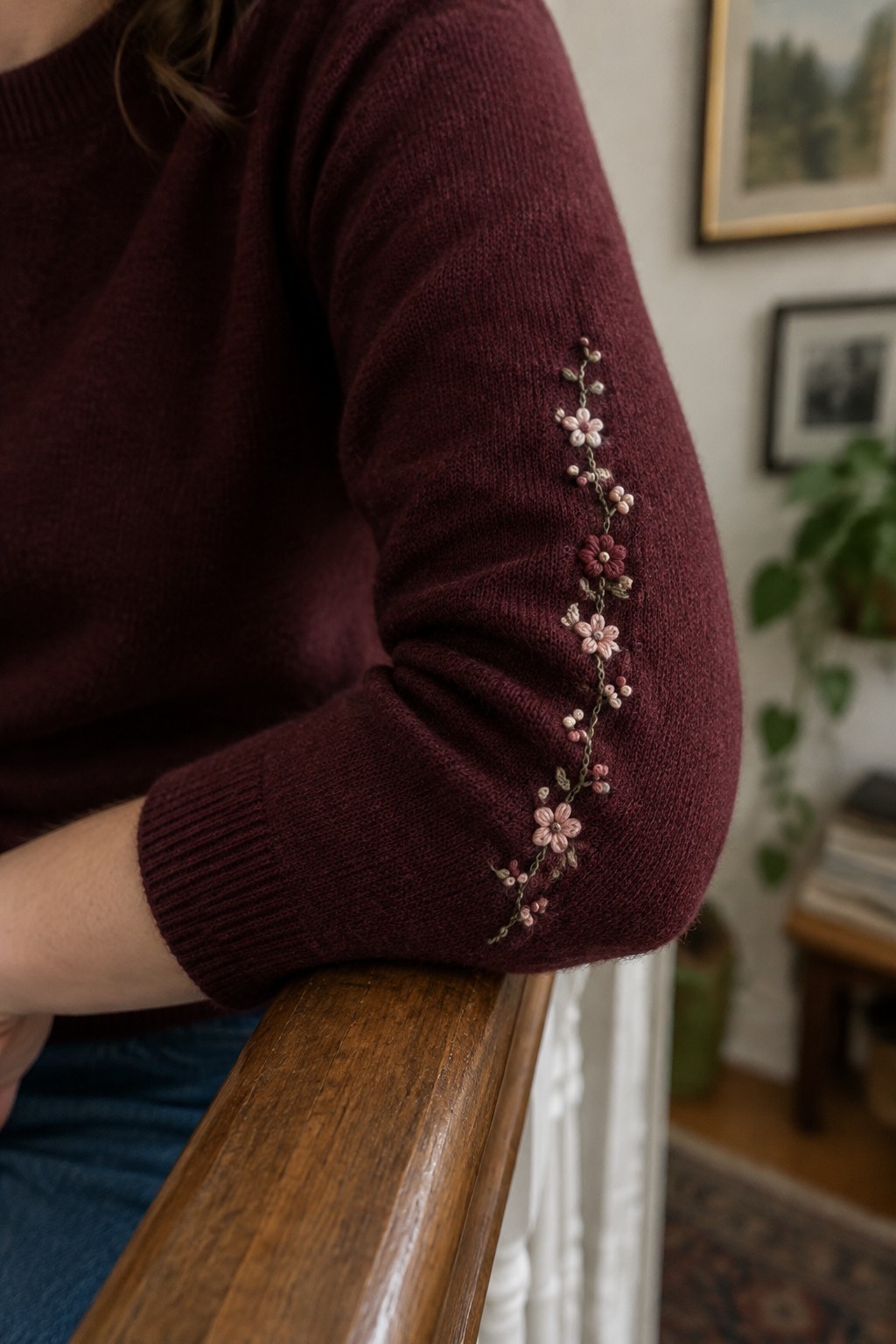 A burgundy sweater sleeve with a small embroidered flower vine curving along the elbow.