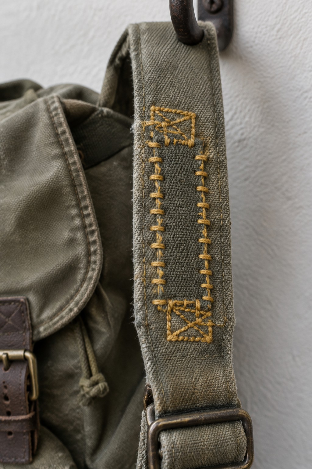 Yellow embroidery reinforces the olive canvas strap of a worn bag.