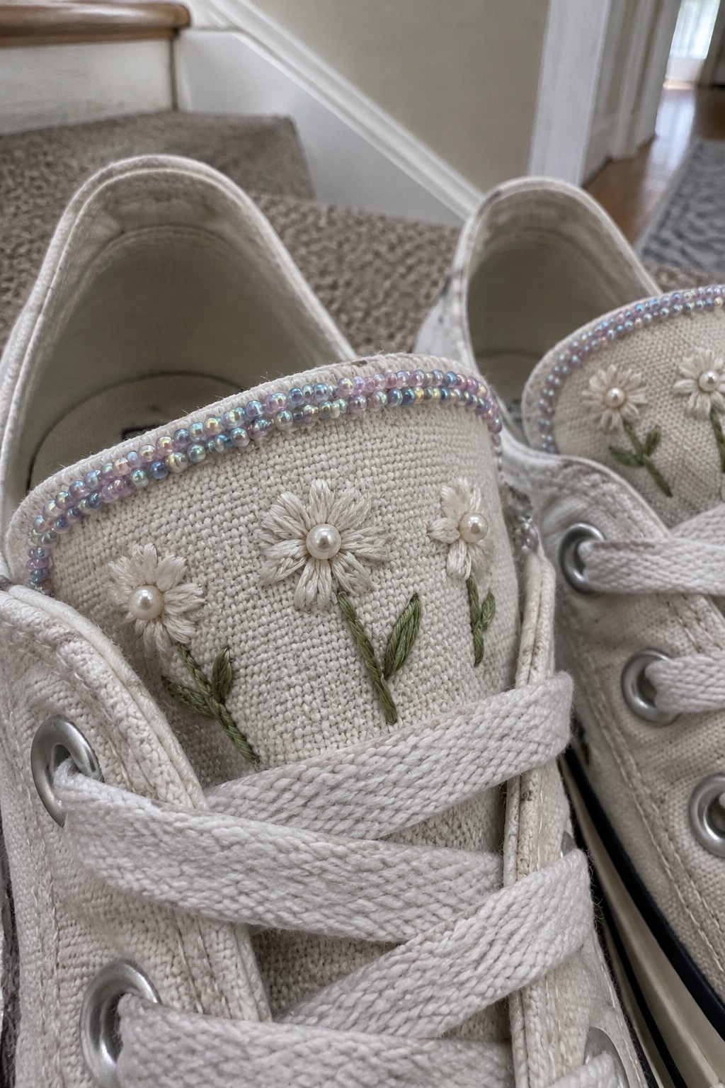 Cream canvas sneakers with embroidered daisies and pearl centers on the tongues, edged with iridescent beads.