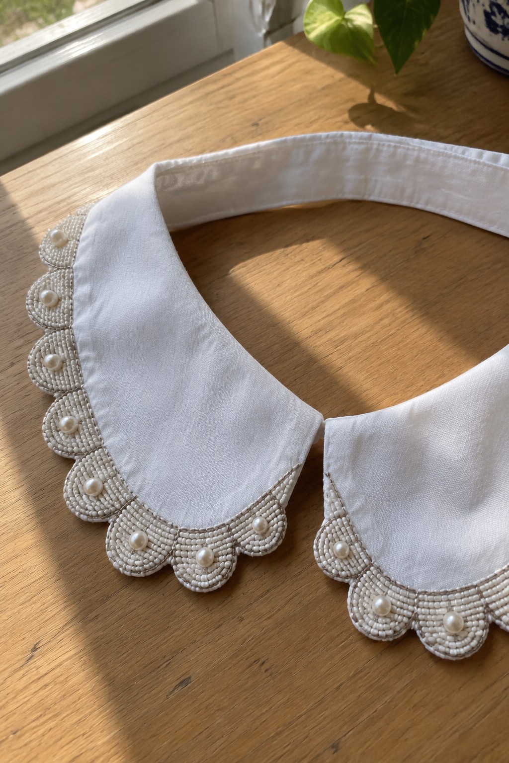 A white fabric collar with scalloped edges embroidered in rows of white beads and accented with pearl-like beads.