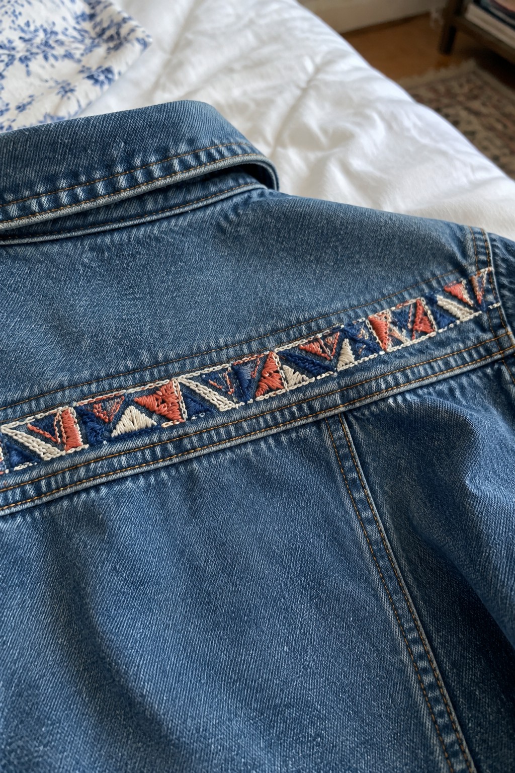 A denim jacket with a multicolored geometric embroidered band across the back.