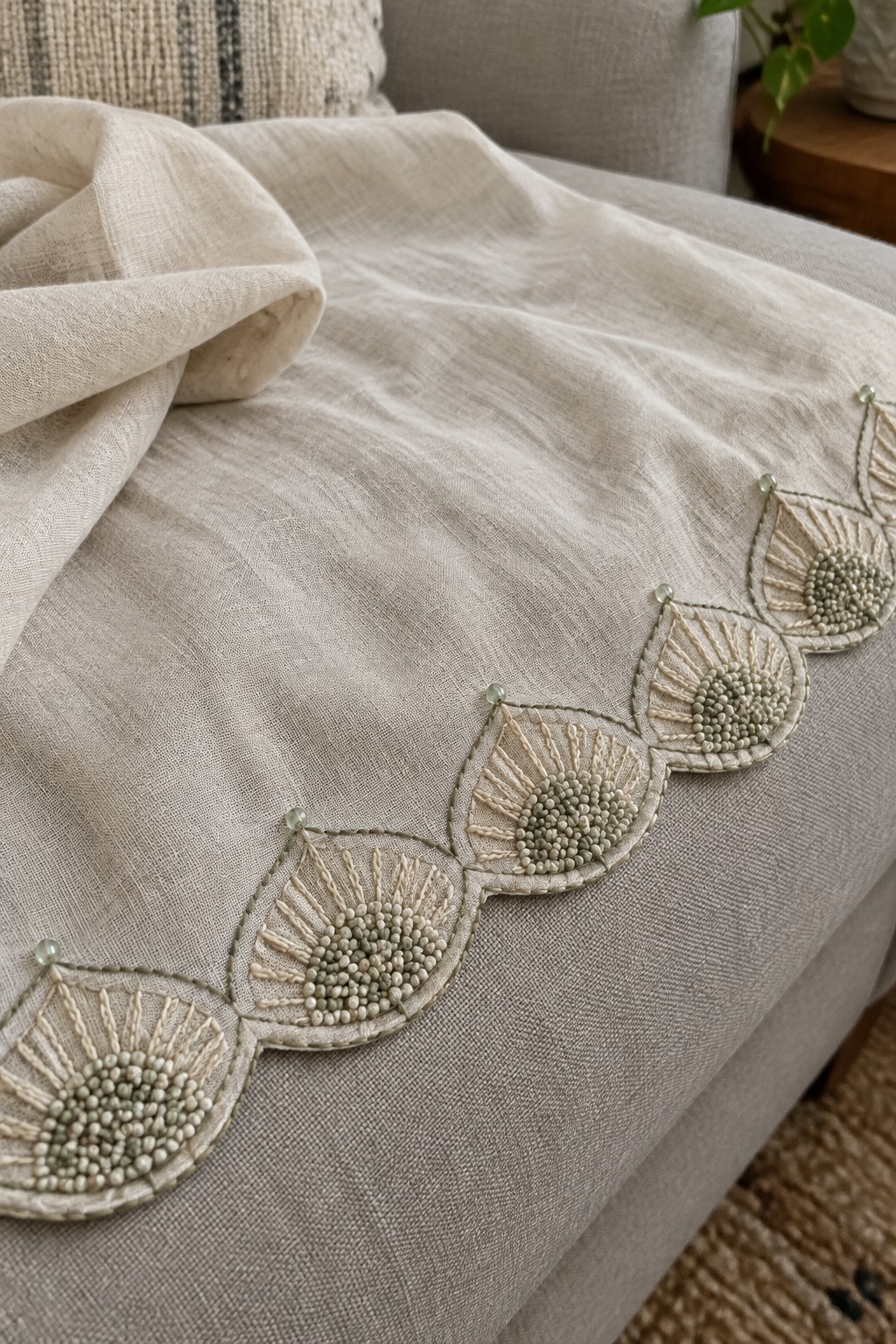 Neutral fabric with a raised beaded scallop embroidery border laid across a sofa.