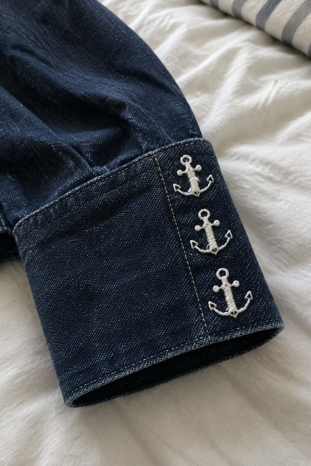 Three small white anchor motifs embroidered in a row on the cuff of dark denim.