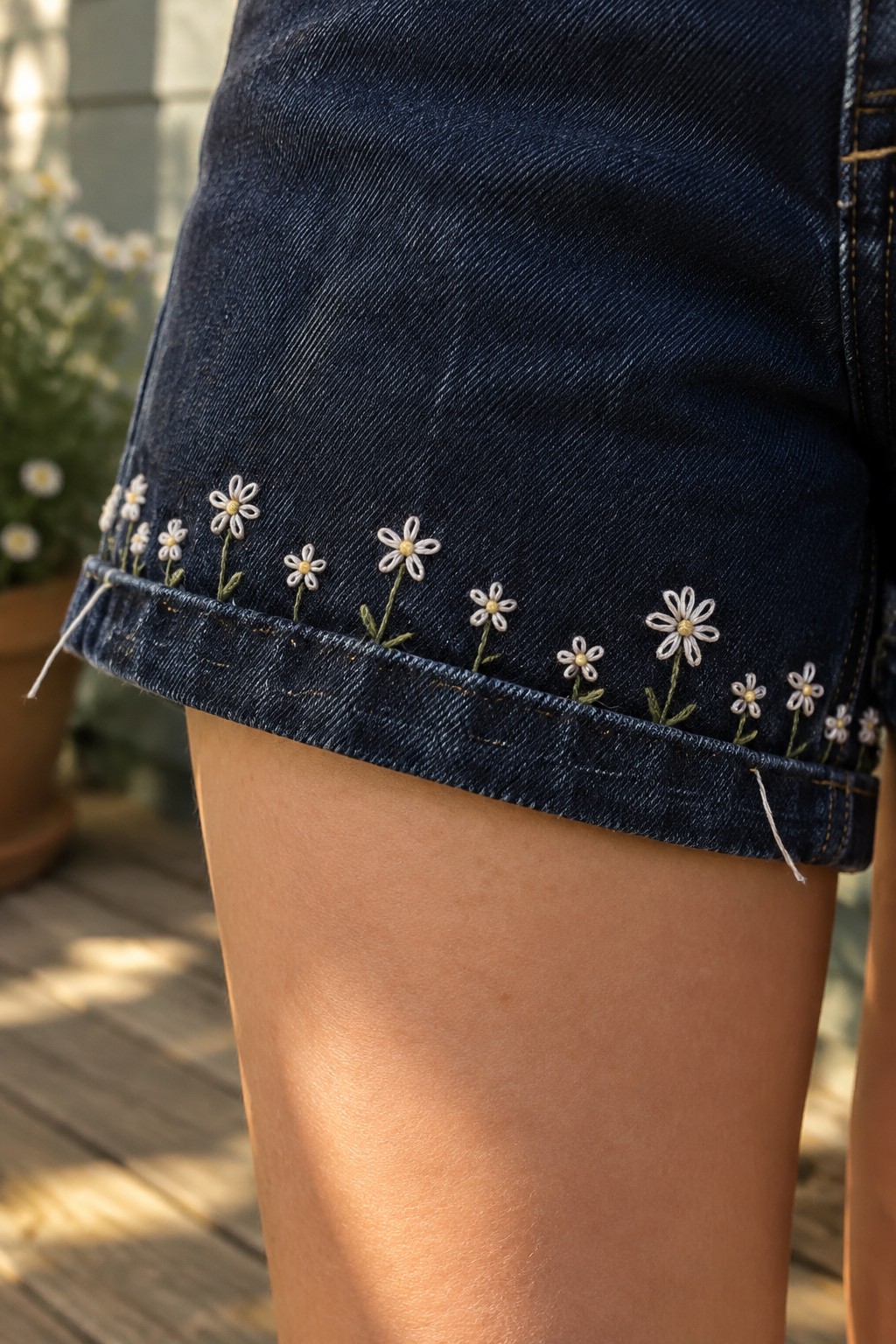 White and yellow daisy embroidery with green stems decorates the cuff of dark denim shorts.