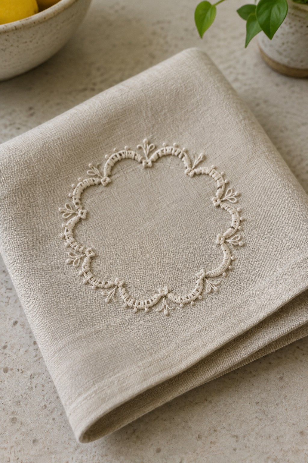 Ivory embroidered round border centered on a folded beige linen napkin.