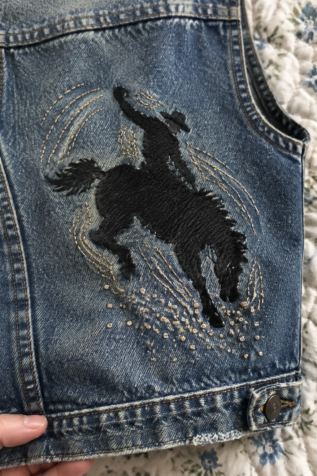 Black embroidered horse silhouette with tan curved stitching on the back panel of a blue denim vest.