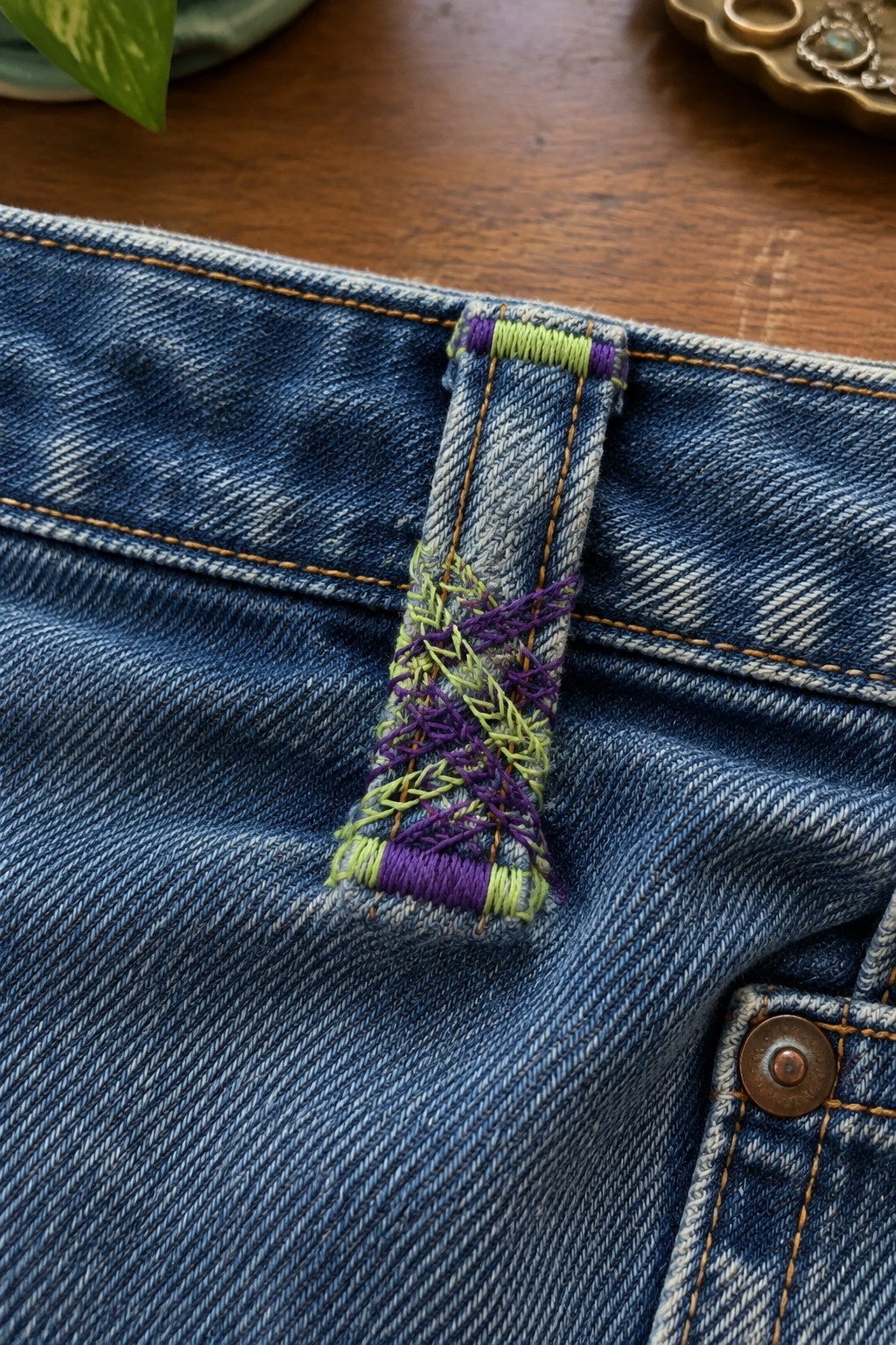 Lime green and purple stitching reinforces a belt loop on blue denim jeans.