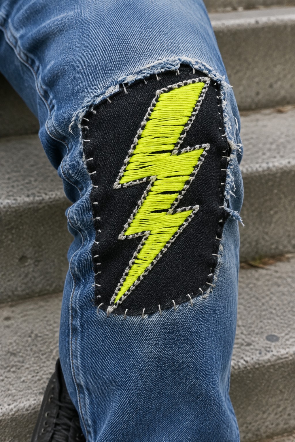 A neon yellow lightning bolt embroidered on a black patch over the knee of blue jeans.