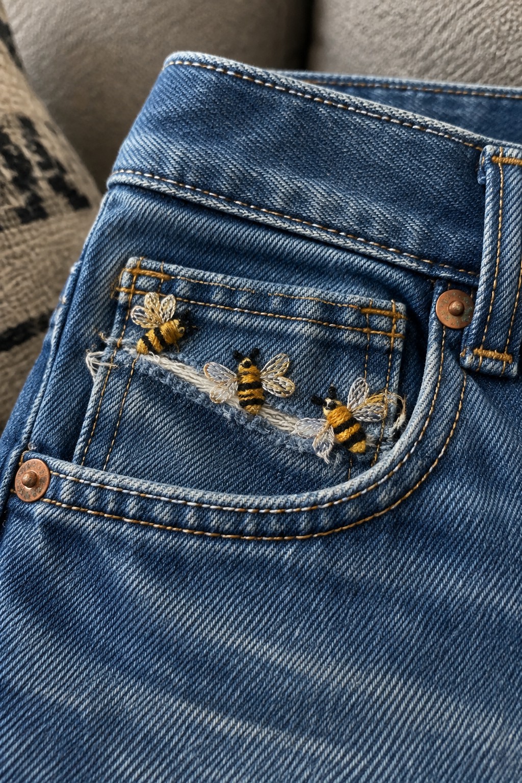 Three embroidered black-and-yellow bees sit along a frayed line on the back pocket of blue jeans.