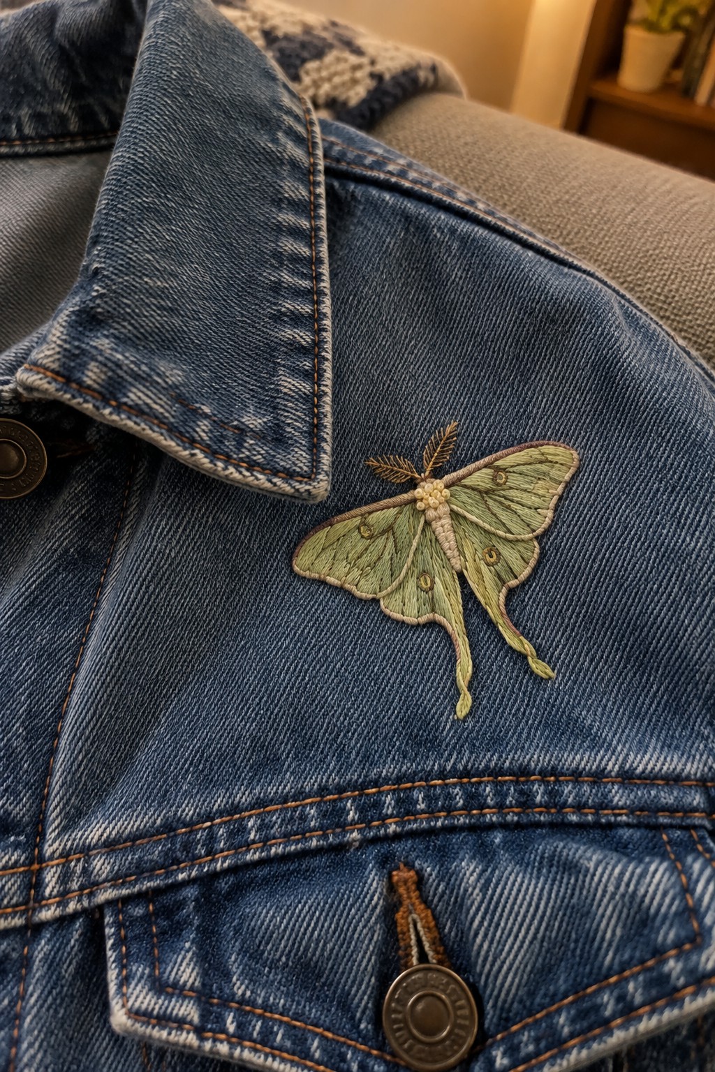 A pale green embroidered luna moth decorates the front of a blue denim jacket.