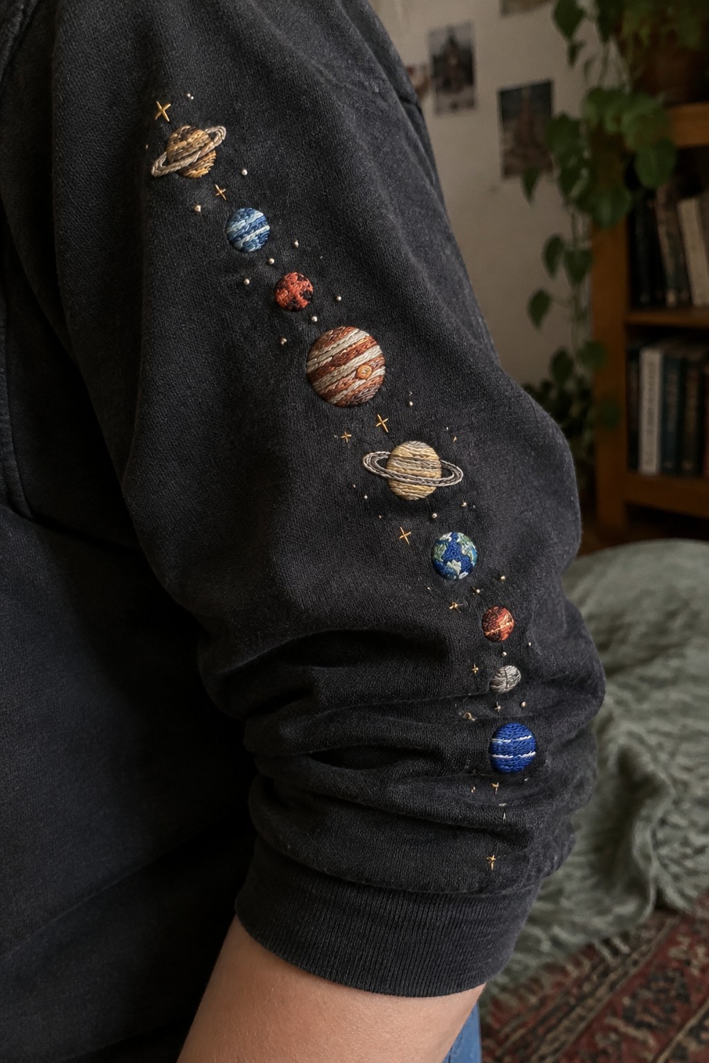 Embroidered planets and small stars run down the sleeve of a dark sweatshirt.