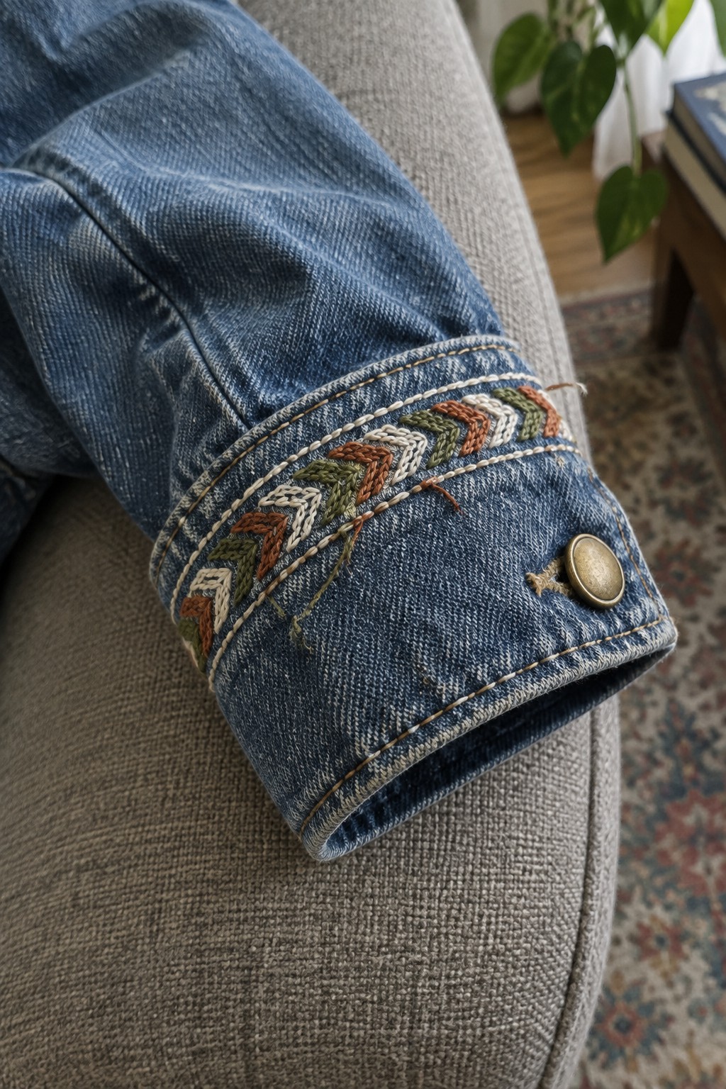 Multicolored chevron embroidery decorates the cuff of a blue denim jacket sleeve.