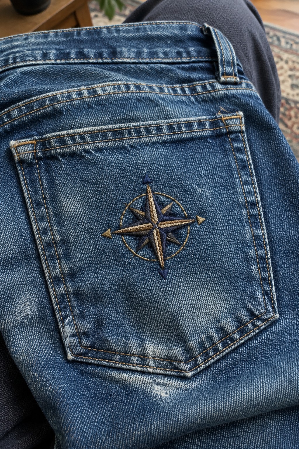 A gold and navy compass rose embroidered on the back pocket of blue jeans.