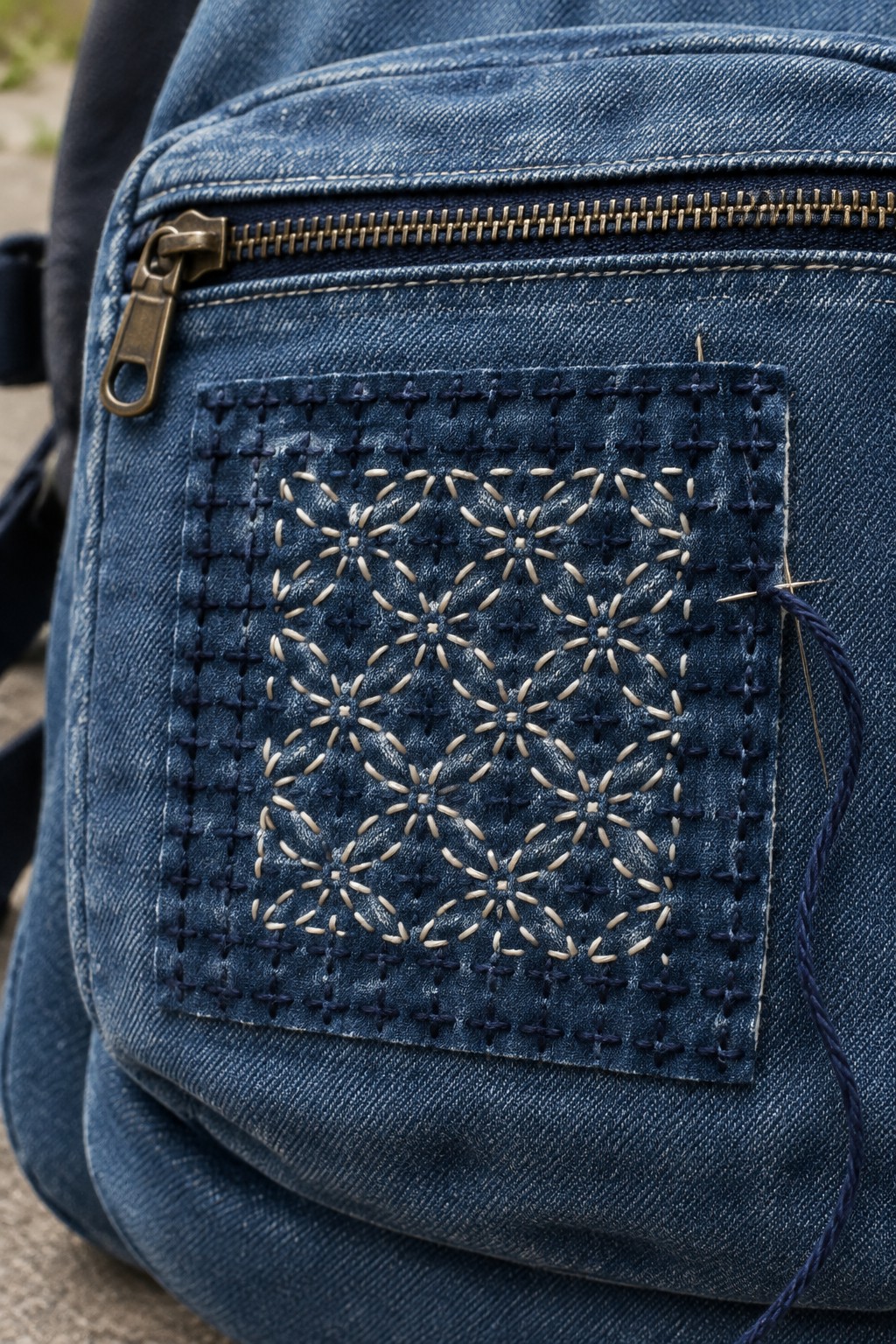 A dark blue denim bag with a pocket decorated in pale radiating stitches and a visible repair patch.