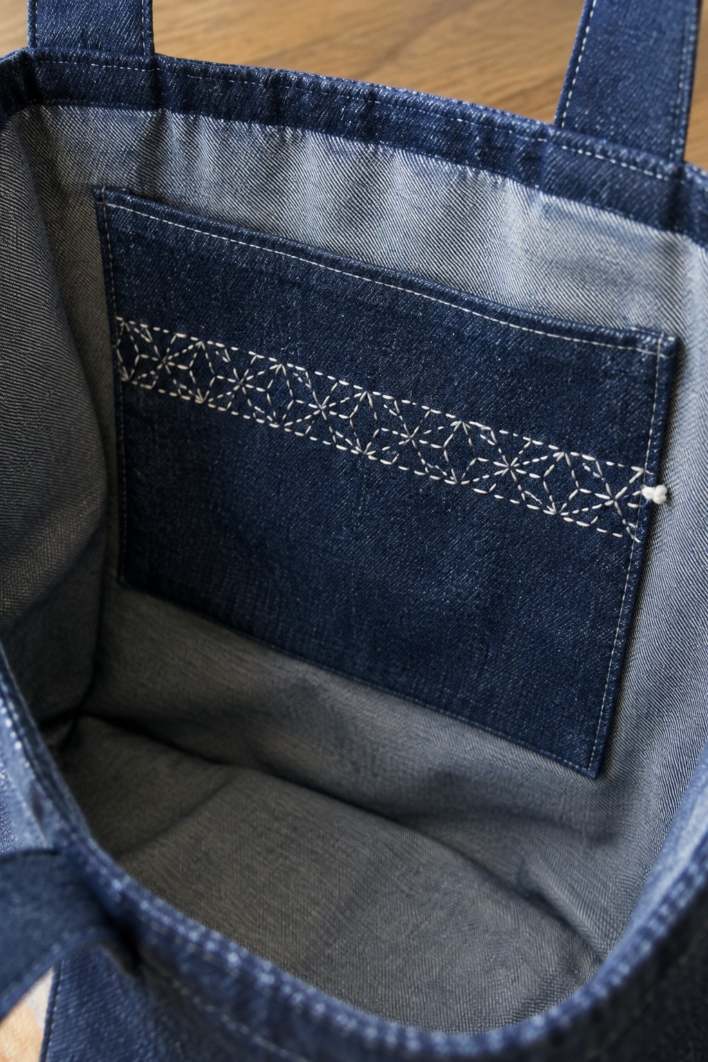 Dark denim tote interior with a pocket decorated with a band of white geometric sashiko stitching.