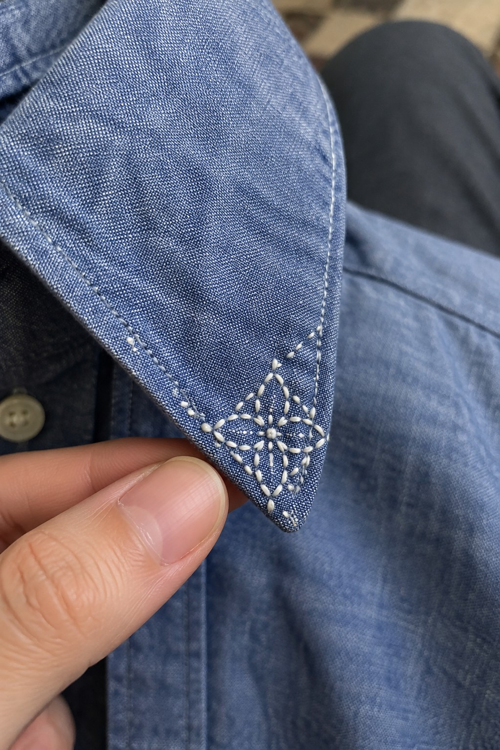 White geometric embroidery decorates the pointed tip of a blue denim collar.