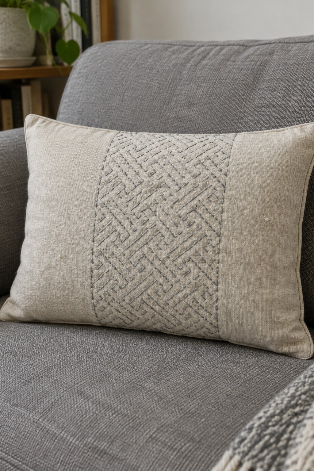 A cream pillow with a wide gray geometric sashiko panel rests on a gray sofa.