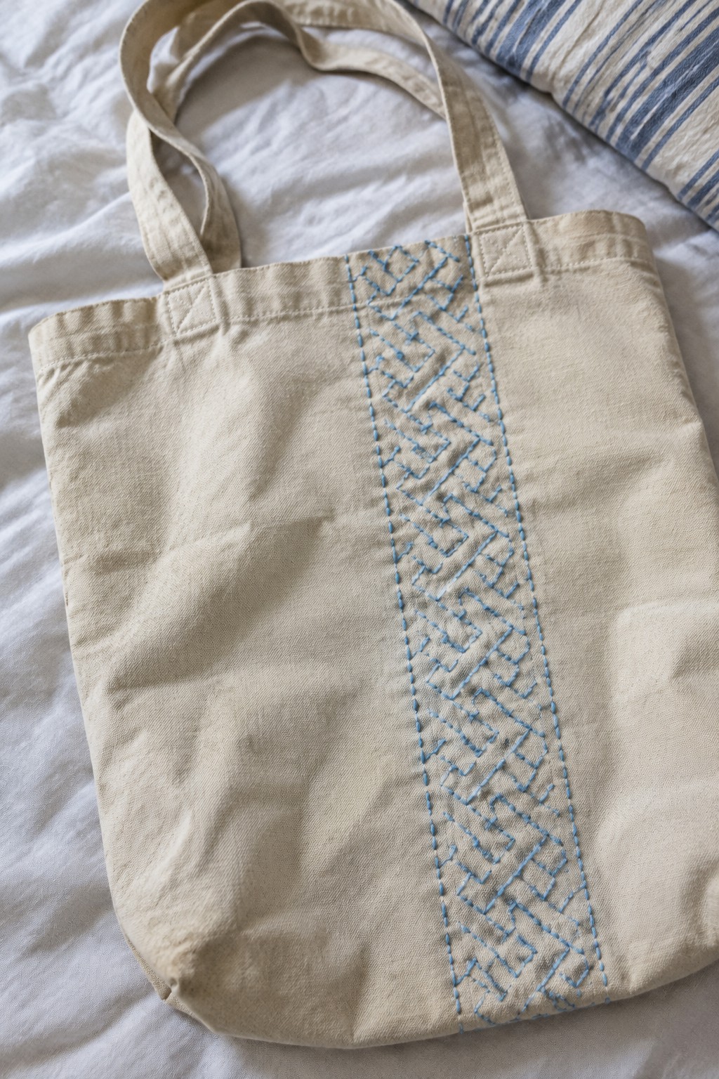 Natural canvas tote with a vertical band of blue geometric embroidery down the front.