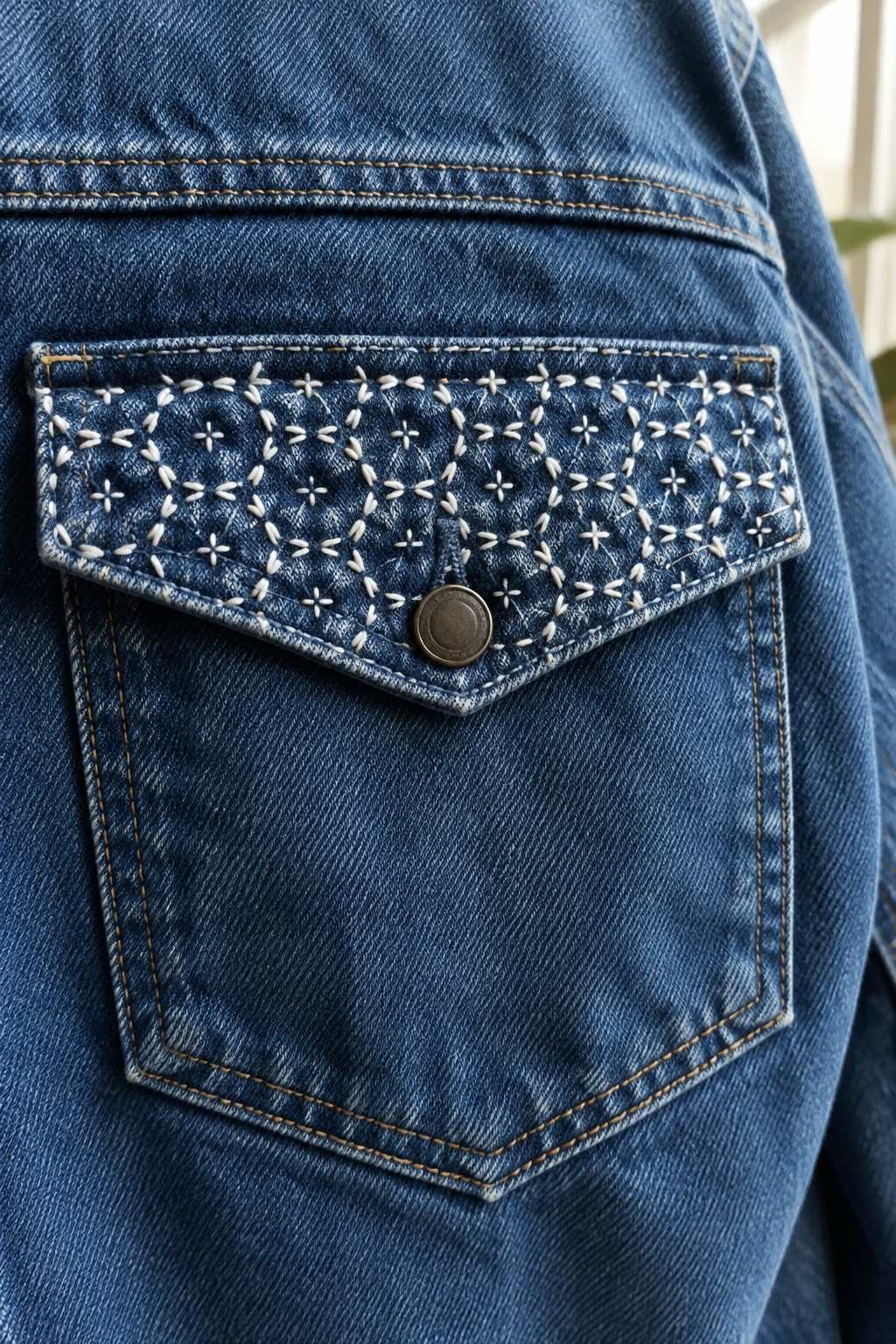White star-like sashiko stitching decorates the flap of a blue denim jacket pocket.