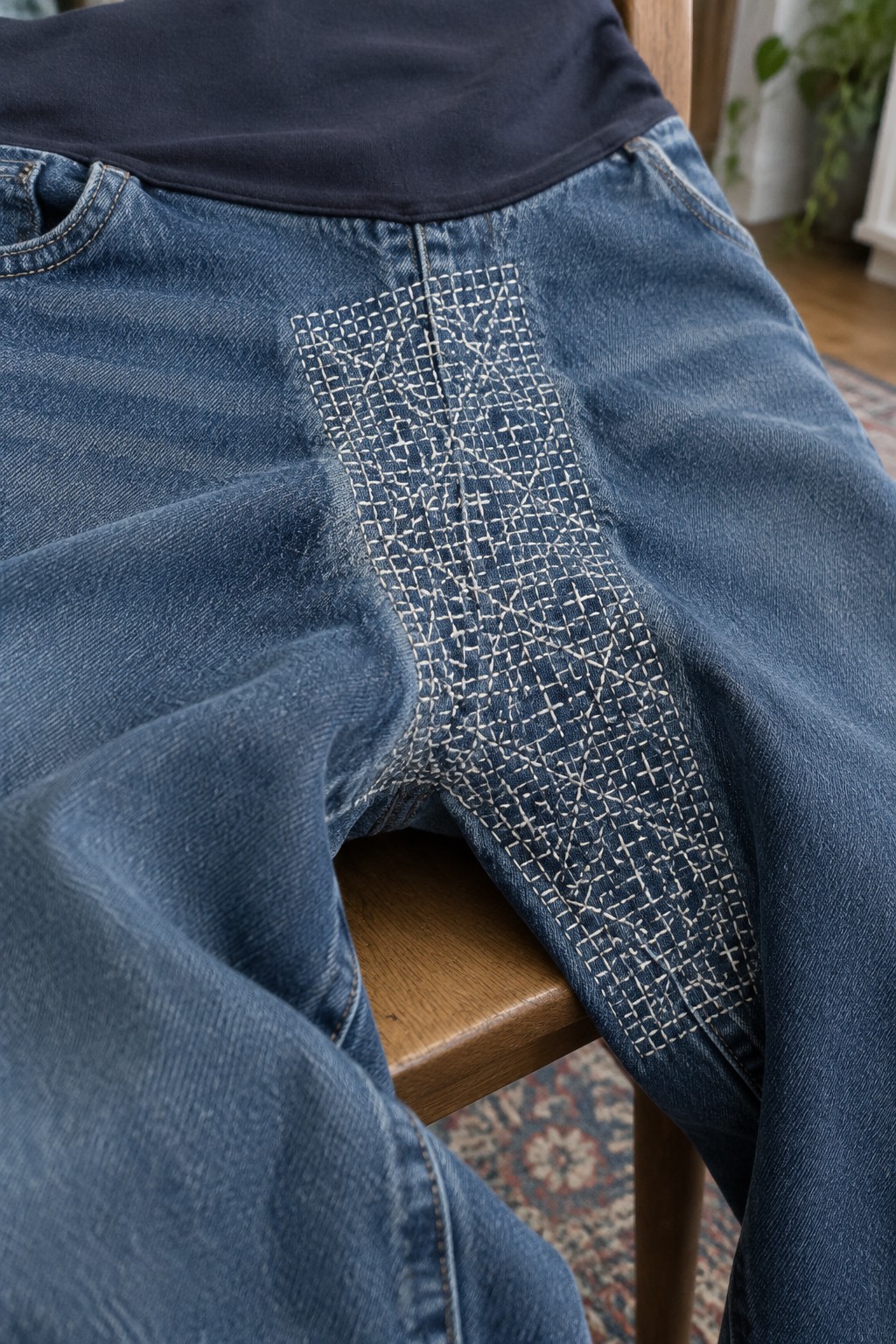 Blue jeans with a dense white geometric sashiko grid stitched across the crotch and upper inner leg.