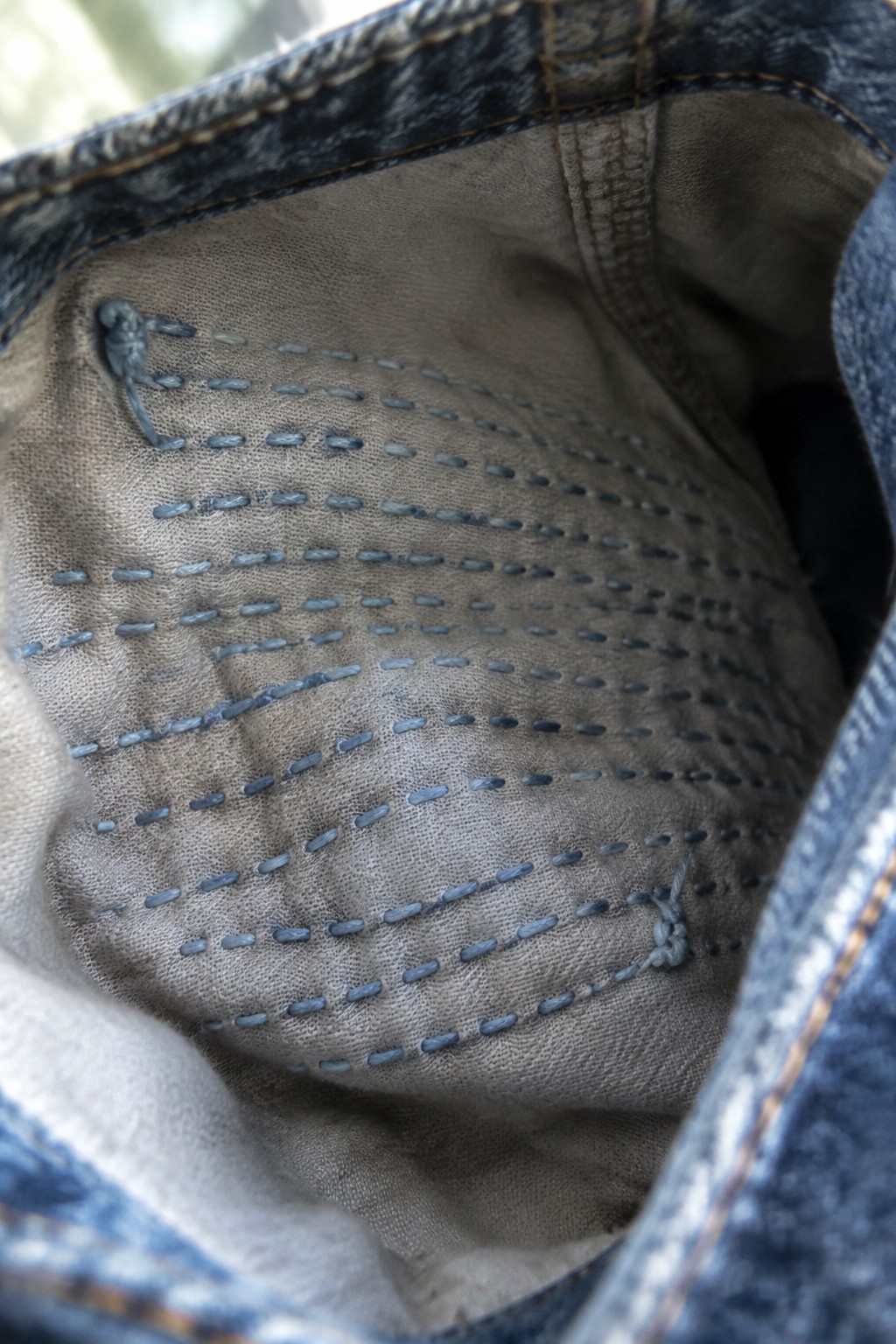 Curved rows of blue stitches reinforce the gray lining inside a denim pocket.