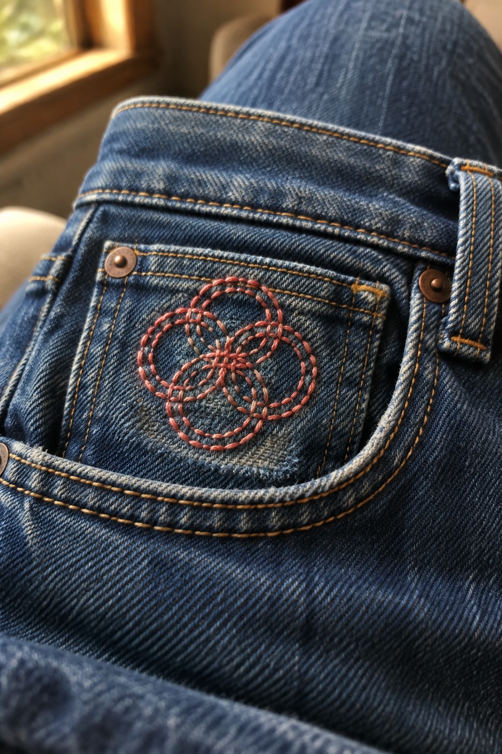 Coral looped flower embroidery decorates the back pocket of blue jeans.