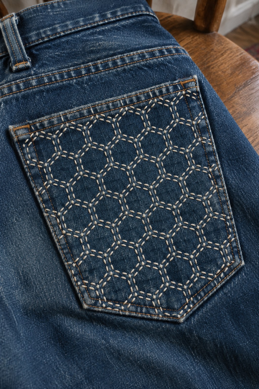 Close-up of a denim back pocket embroidered with a repeating geometric pattern in pale thread.
