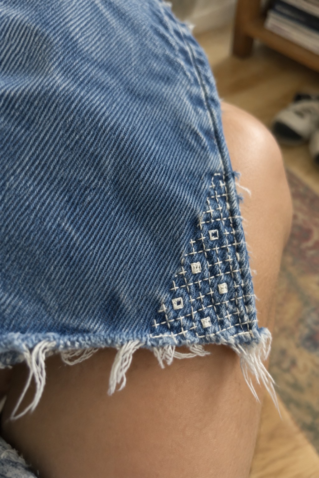 White geometric sashiko stitching decorates the frayed hem of blue denim shorts.