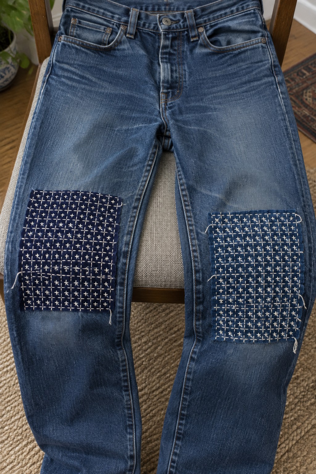 Blue jeans laid flat with rectangular navy patches covered in white geometric stitching over both knees.