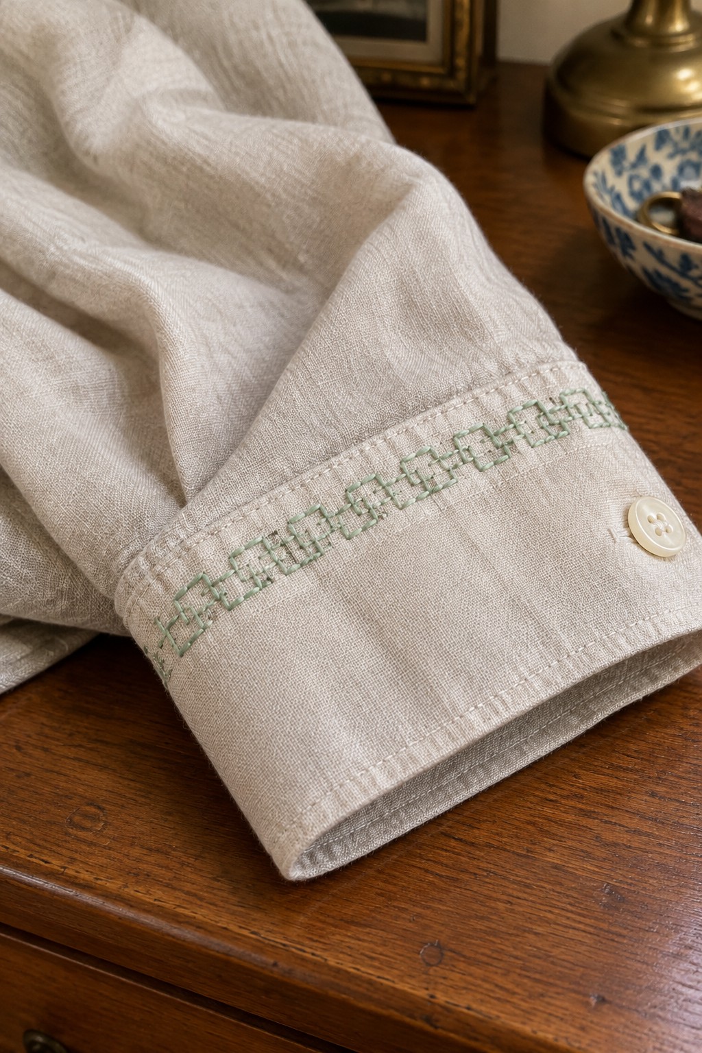 A beige linen cuff with a repeating green geometric embroidery band and a white button.