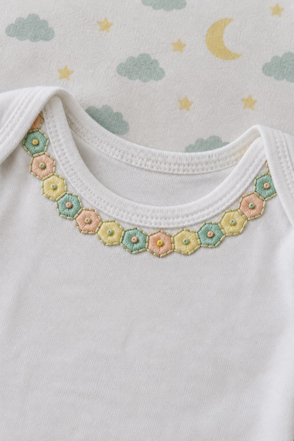 White top with a rounded neckline bordered by pastel hexagonal embroidered flowers.