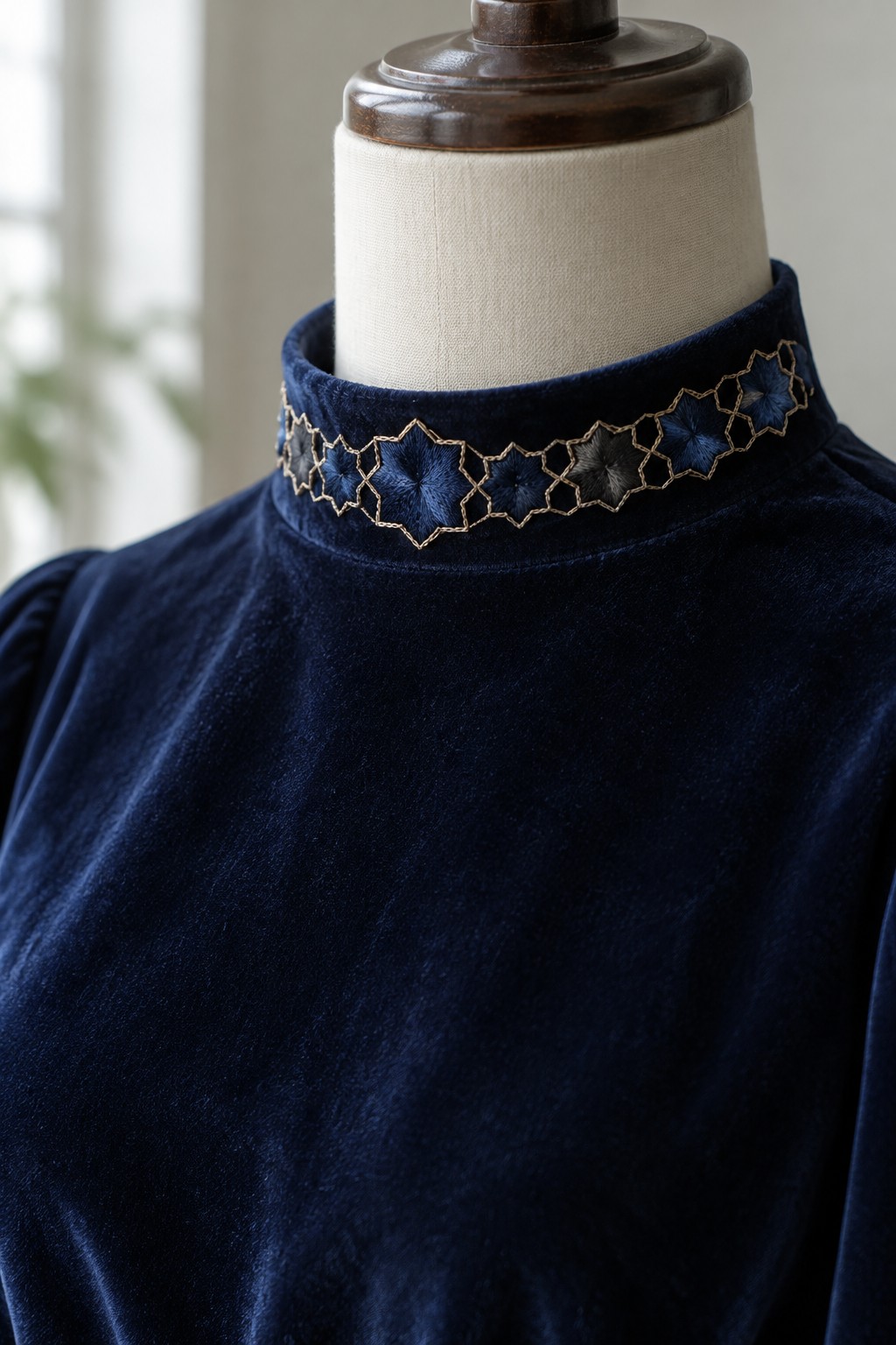 A navy velvet garment on a dress form with blue starburst embroidery and pale geometric outlines around its raised collar.