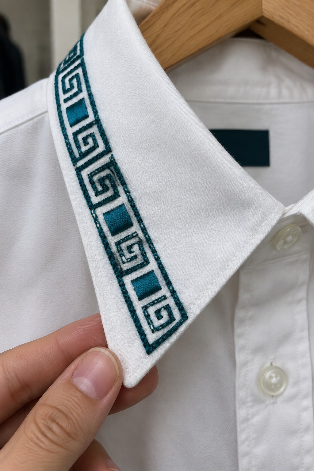A white shirt collar with a teal geometric Greek key and square border embroidered along its edge.